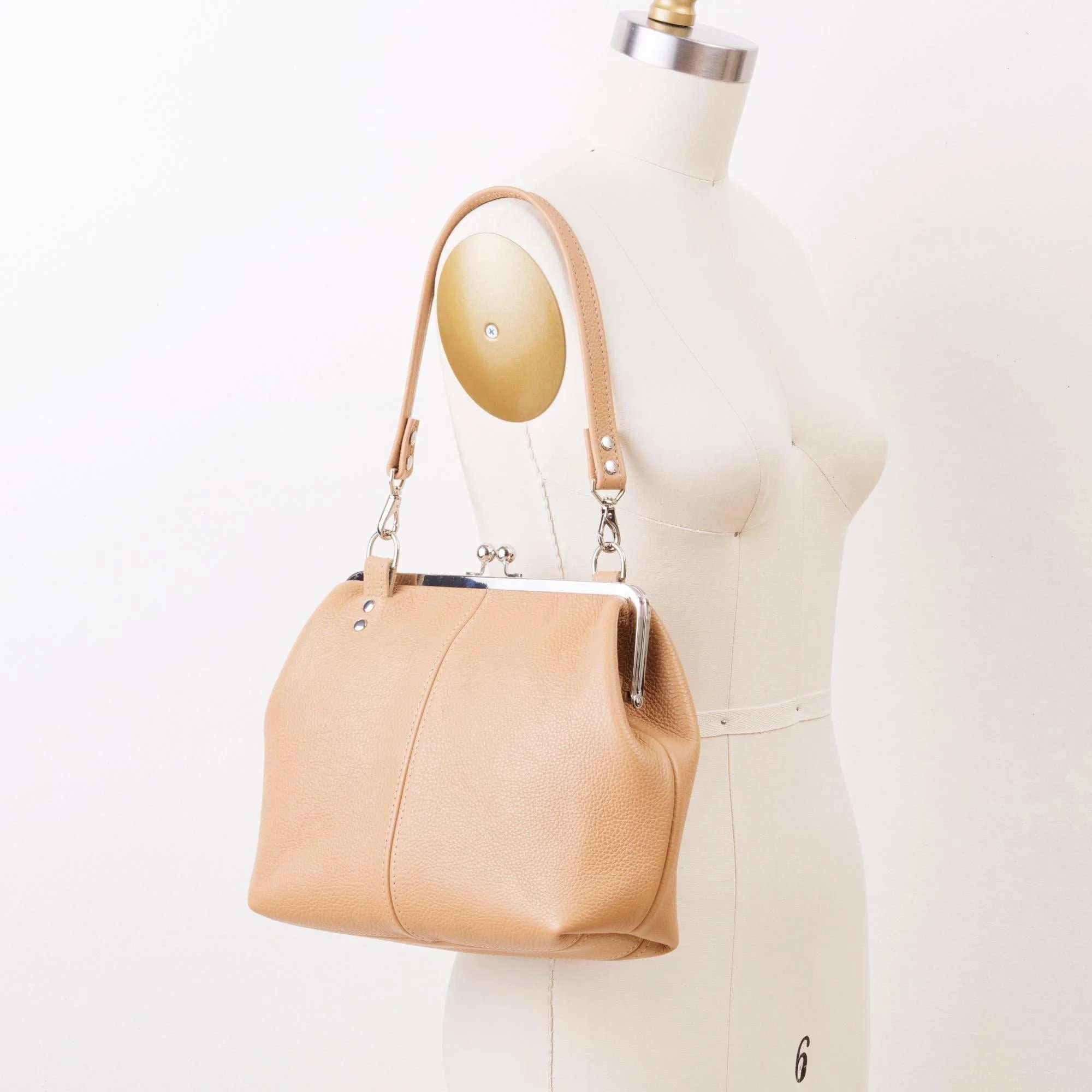 Tan pebble grain leather kiss lock handbag with silver finish hardware and shorty shoulder strap on mannequin.