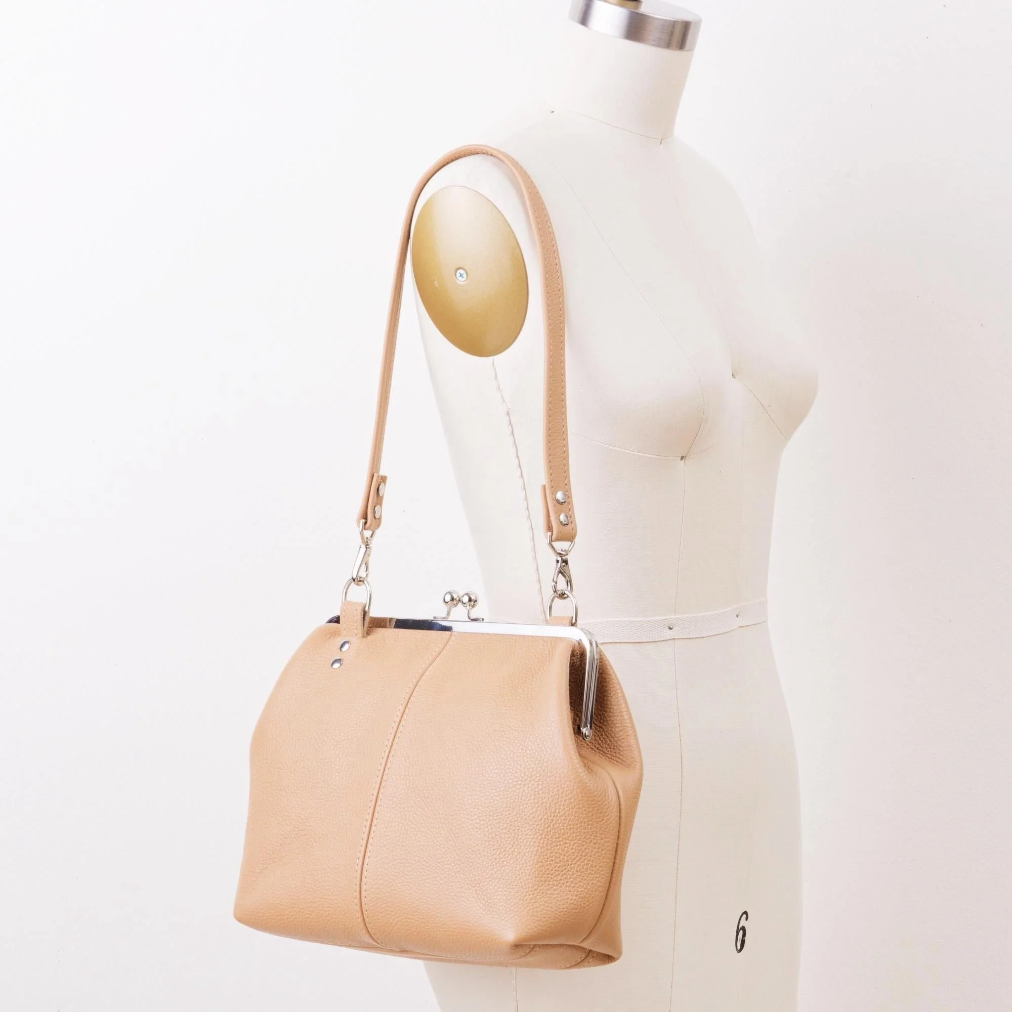 Tan pebble grain leather kiss lock handbag with silver finish hardware and standard shoulder strap on mannequin.