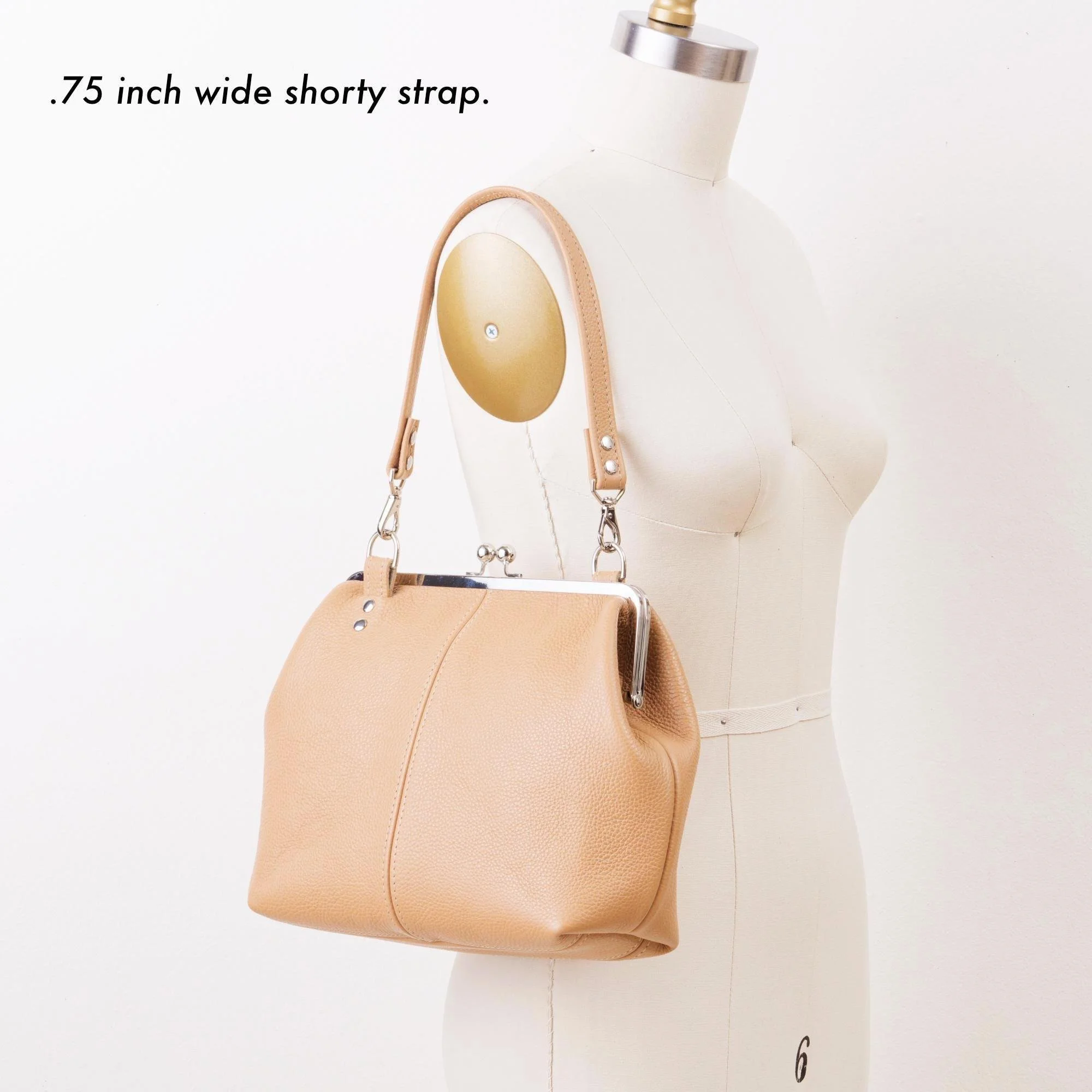 Tan pebble grain leather kiss lock handbag with silver finish hardware and shorty shoulder strap on mannequin with strap description.