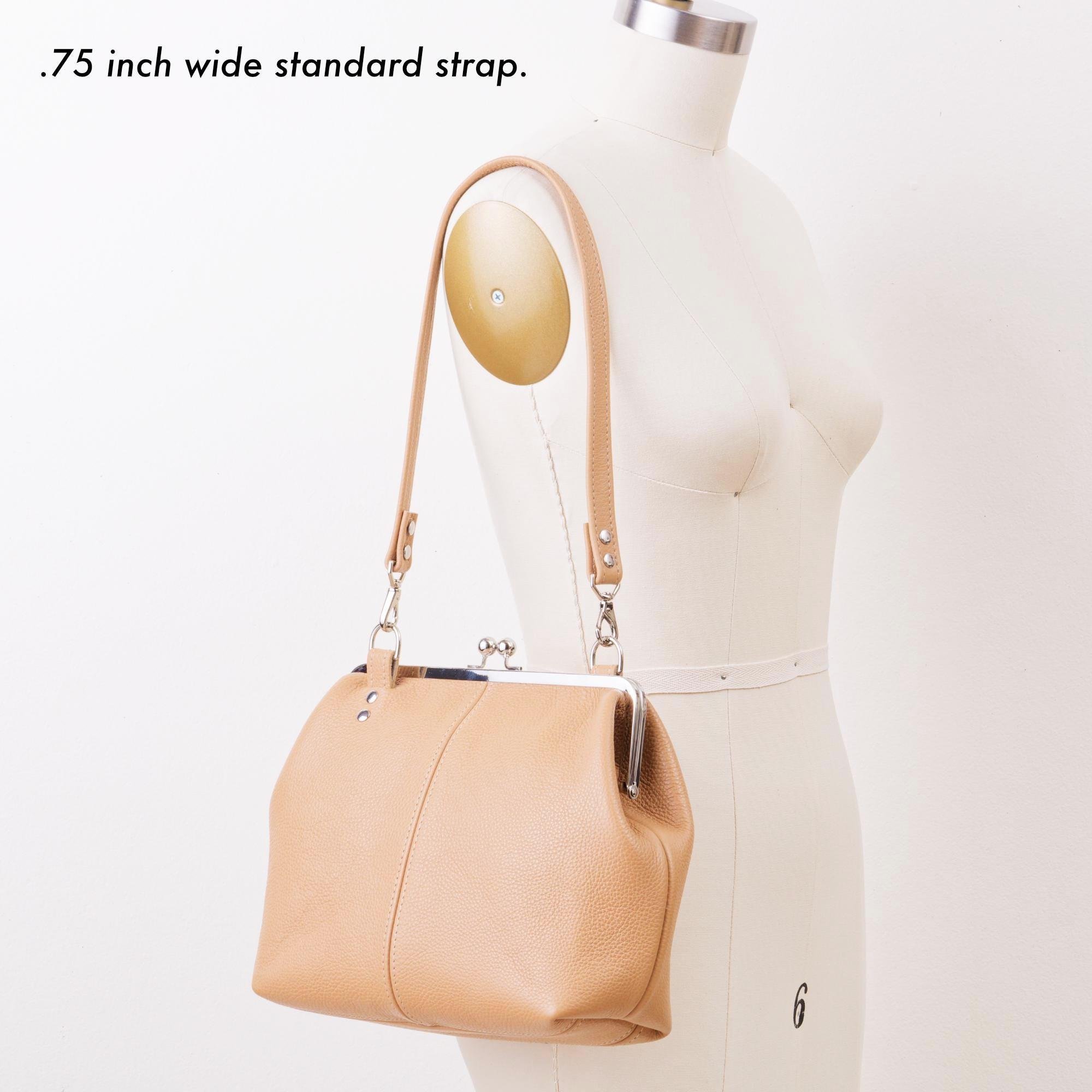 Tan pebble grain leather kiss lock handbag with silver finish hardware and standard shoulder strap on mannequin with strap description.