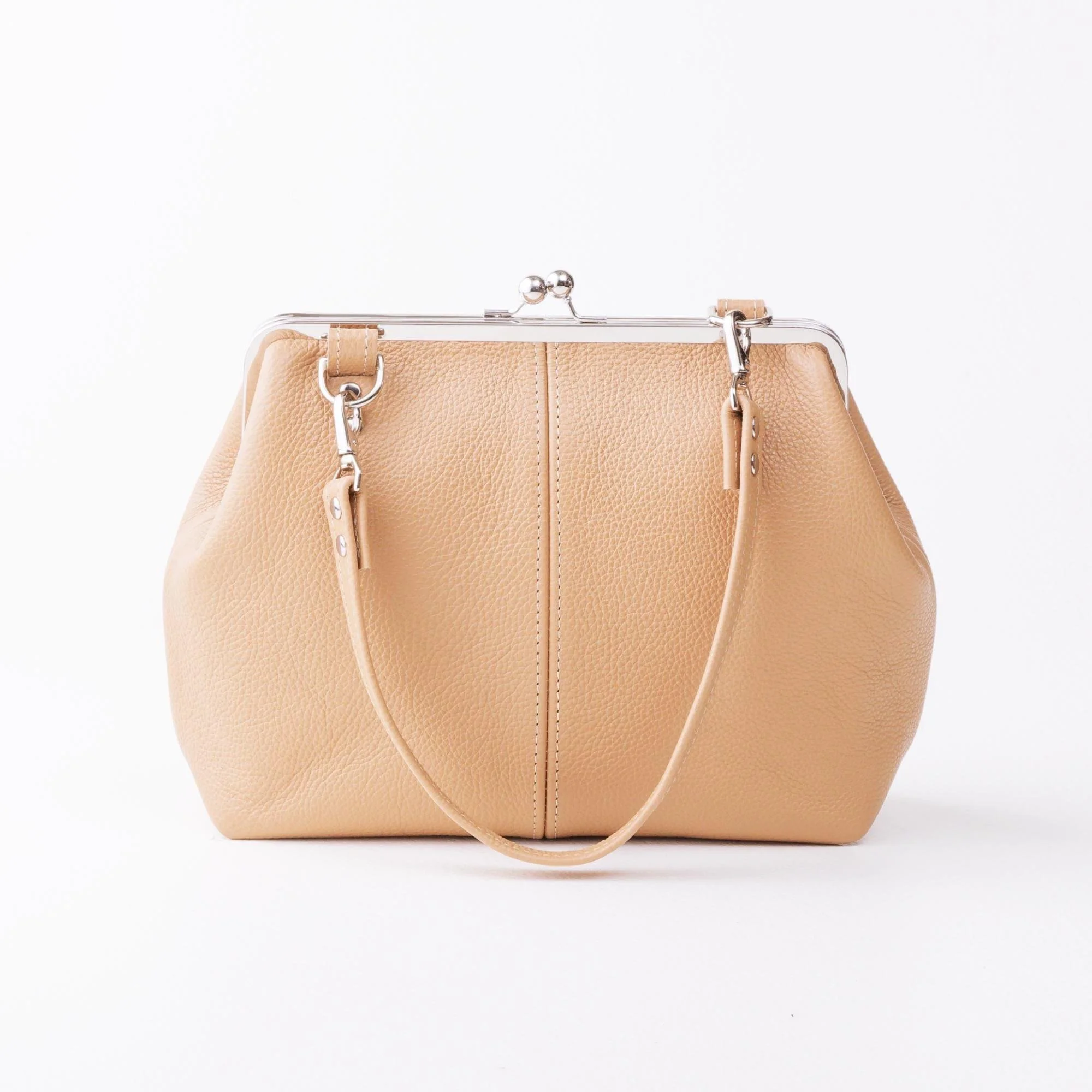 Front view of tan pebble grain leather kiss lock handbag with silver finish hardware and shorty shoulder strap on tabletop with strap down.