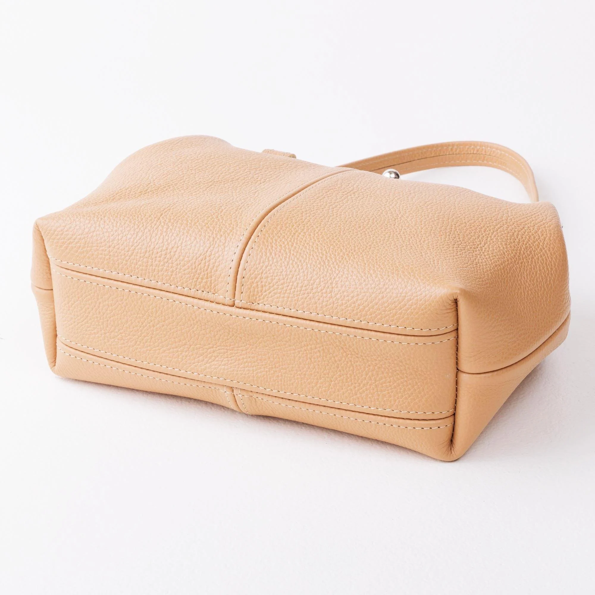 Bottom view of tan pebble grain leather kiss lock handbag on tabletop.