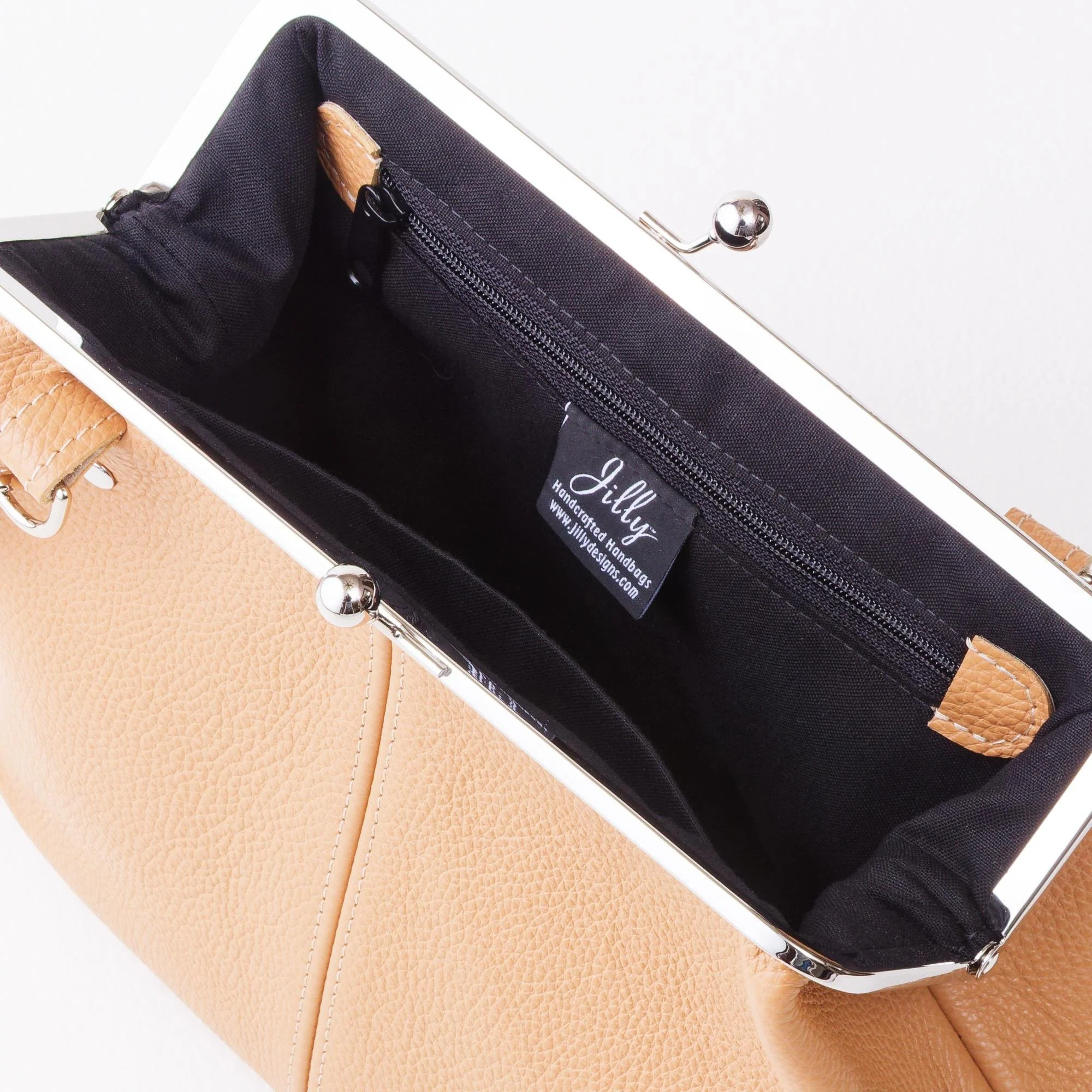 Interior view of tan pebble grain leather kiss lock handbag with silver finish hardware, zipper pocket and slip pocket.