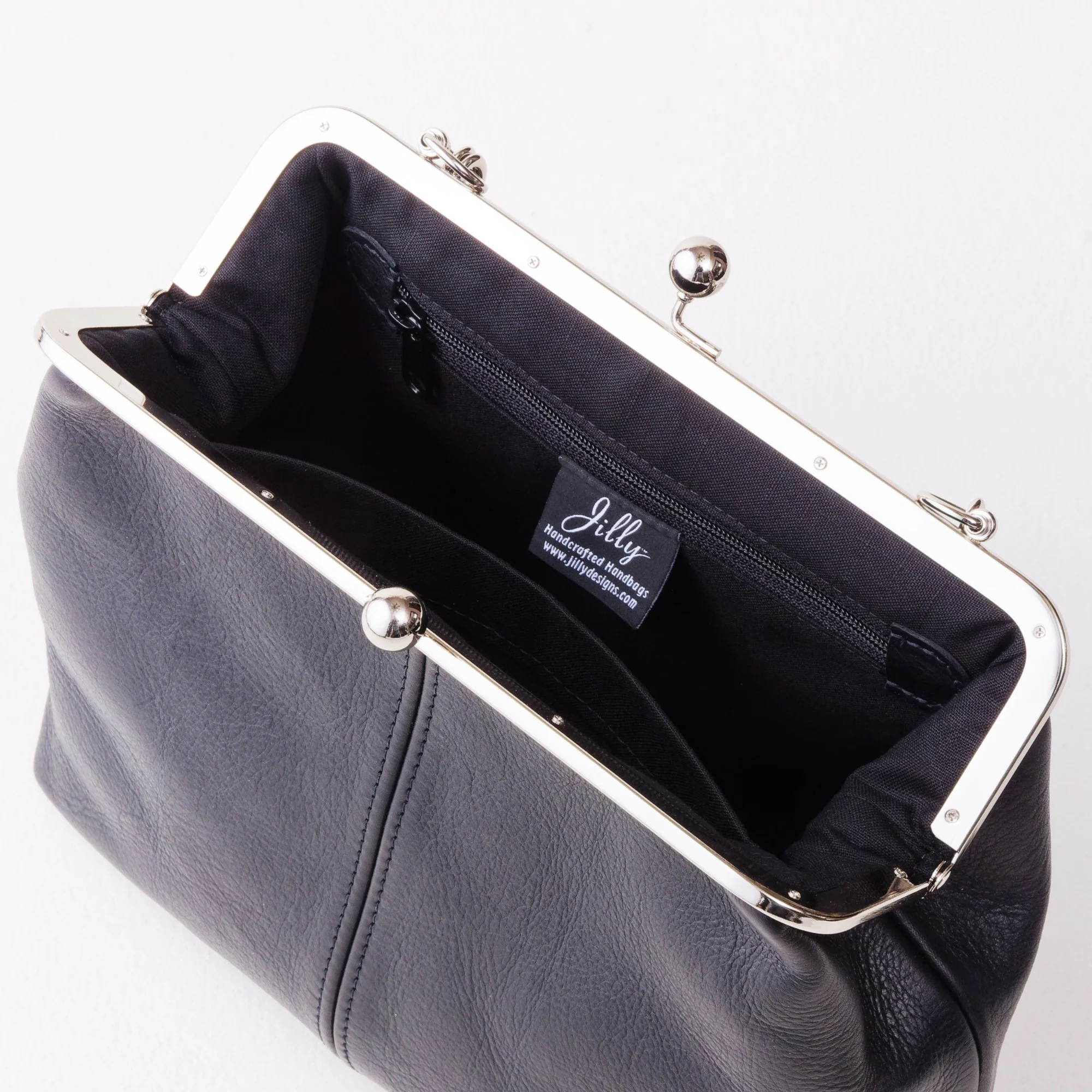 Interior view of black leather kiss lock handbag with silver finish hardware, zipper pocket and slip pocket.