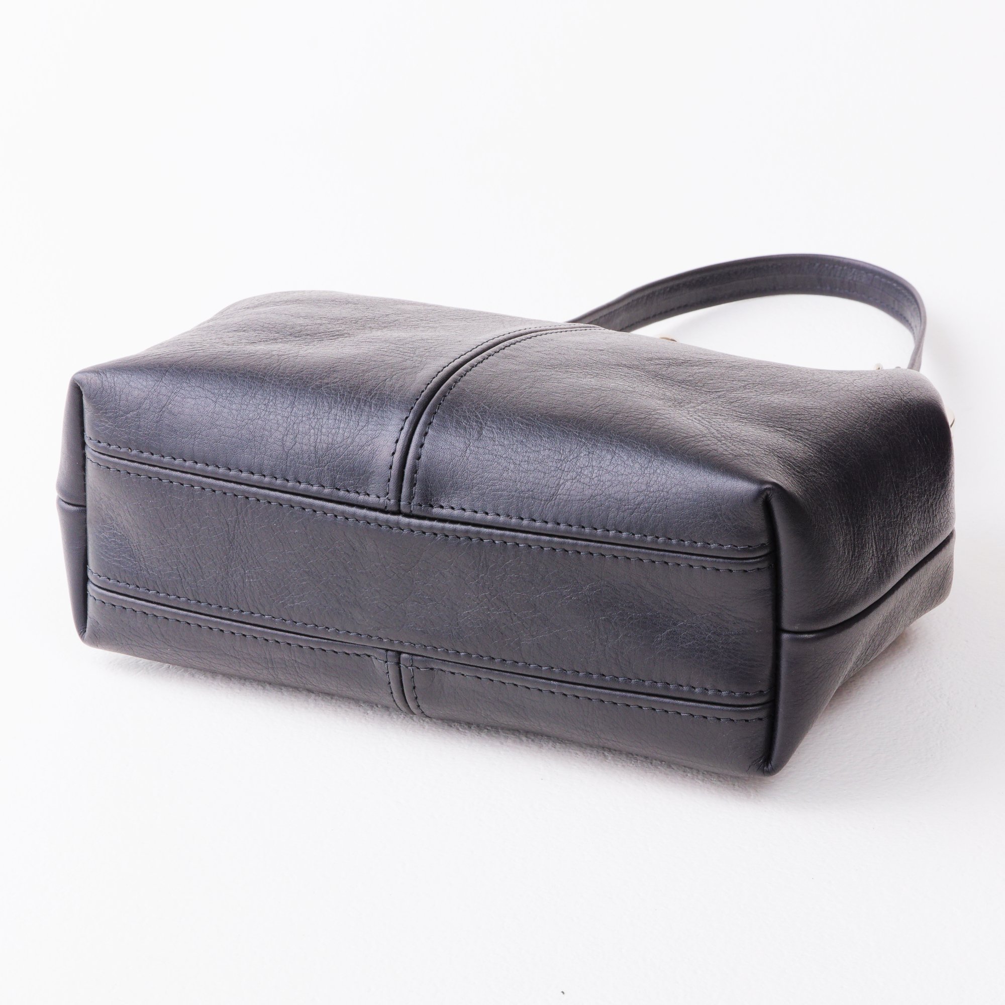 Bottom view of black leather kiss lock handbag on tabletop.