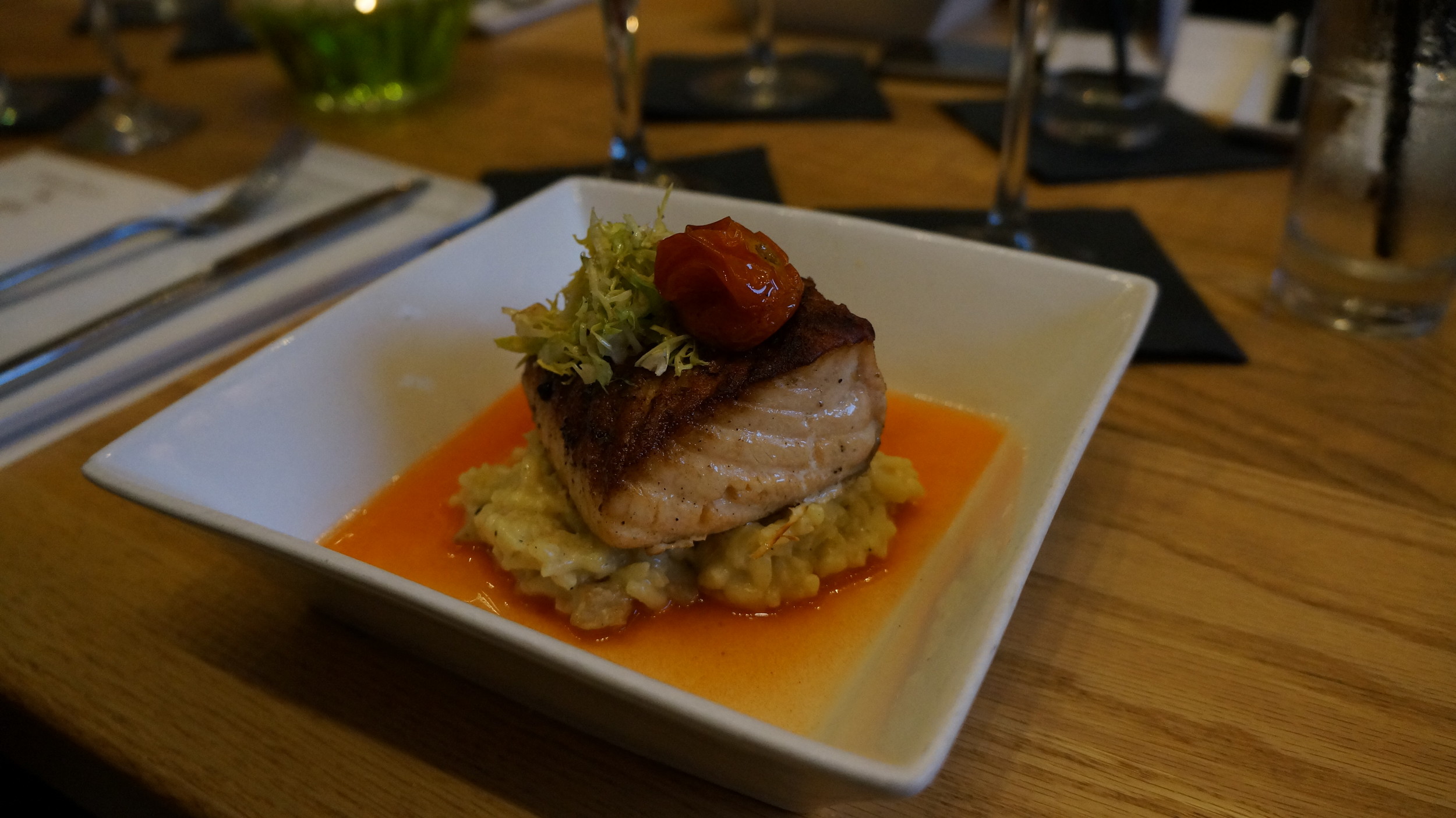 Pan Seared Salmon: The salmon is seasoned with salt and pepper, then pan seared. It is paired with a creamy ratatouille risotto, containing roasted eggplant, sautéed zucchini, and roasted tomatoes. The risotto rests in a sweet red pepper consumme (broth), and the salmon adorns the dish. 