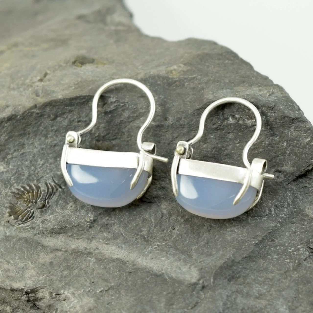 Turkish Blue Chalcedony Hoops 

This is a new style of earring mechanism for me. I really wanted to display the irregularly cut stones in a way that let them drop horizontally, and this design was what I came up with. The open-top settings let light 