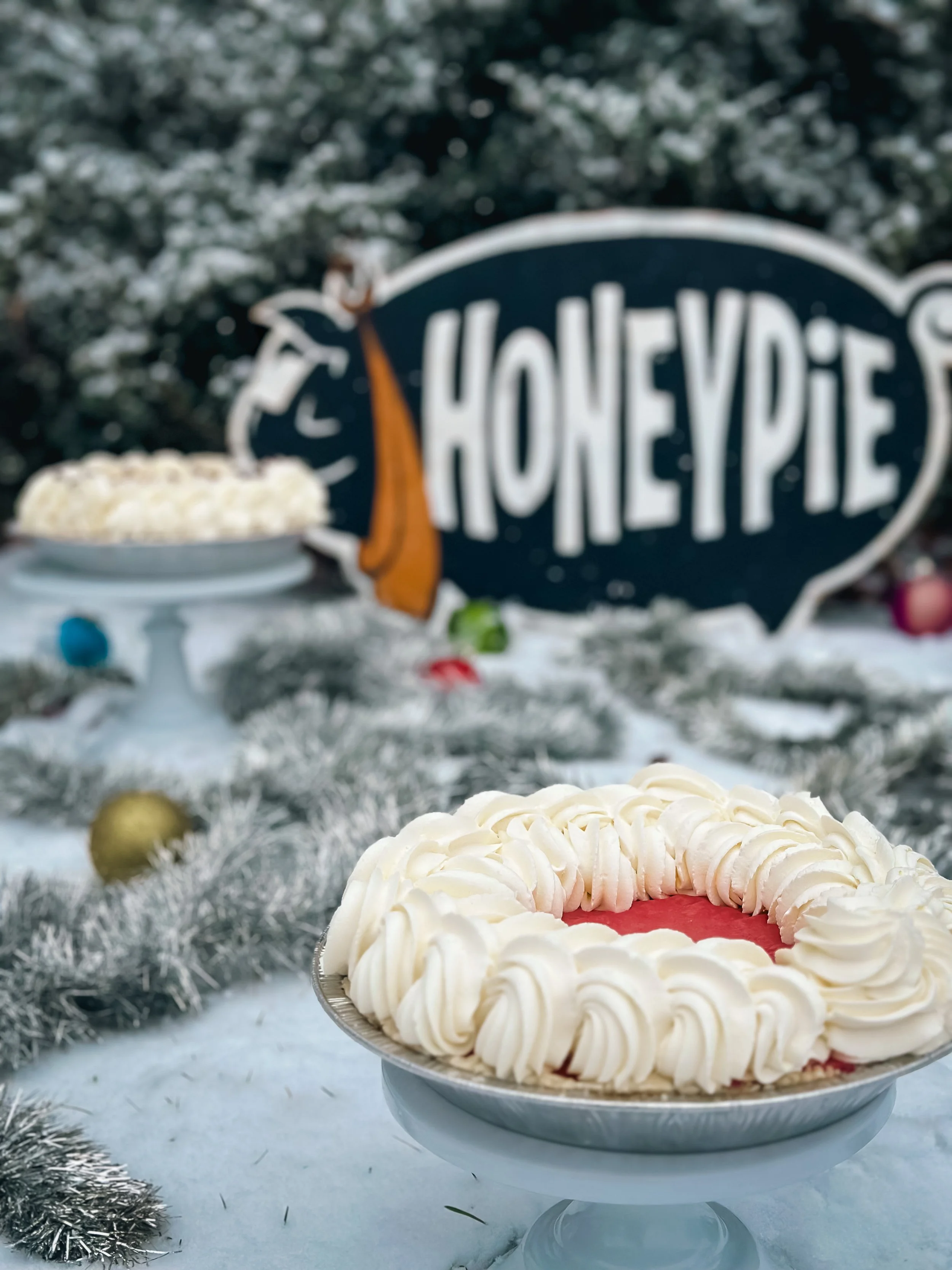Cranberry cream pie in front of the Honeypie sign with snow and Christmas decorations.