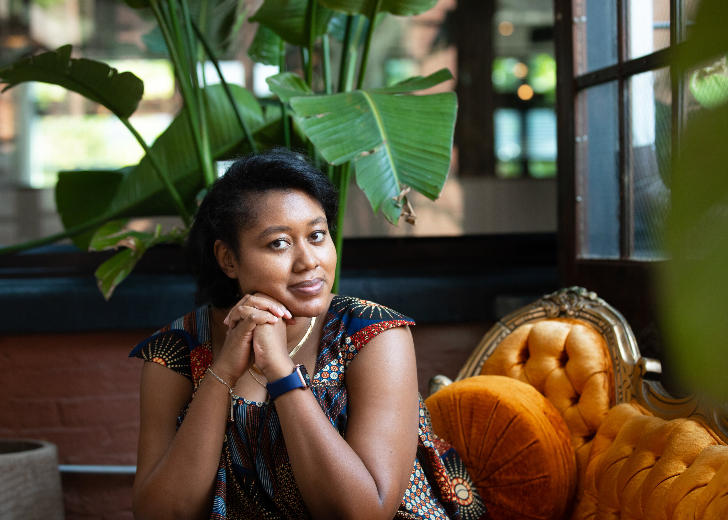 Zakiya Whatley, PhD, science communicator and storyteller, sitting on orange couch with hands folded