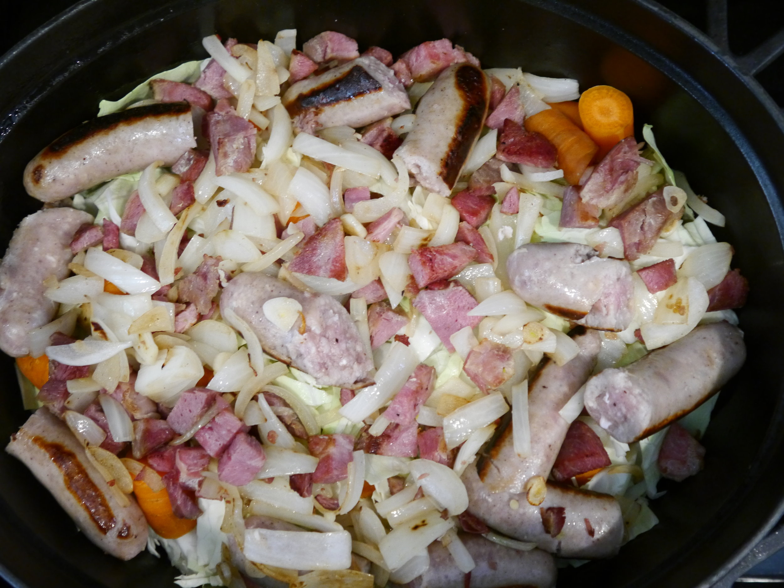 Layer cabbage and carrots on top of potatoes and then sausages, bacon, onion and garlic.