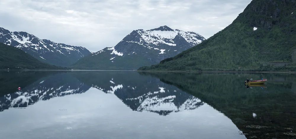 A boat in a Norwegian fjord with mountains reflecting off water.
