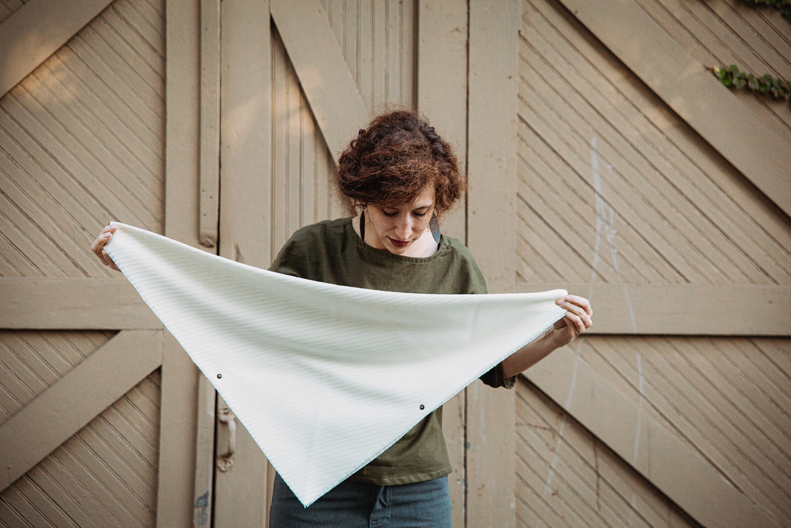 Start by holding the cowl in front of you; fringed point pointing down, leather tab in each hand and snap components facing out