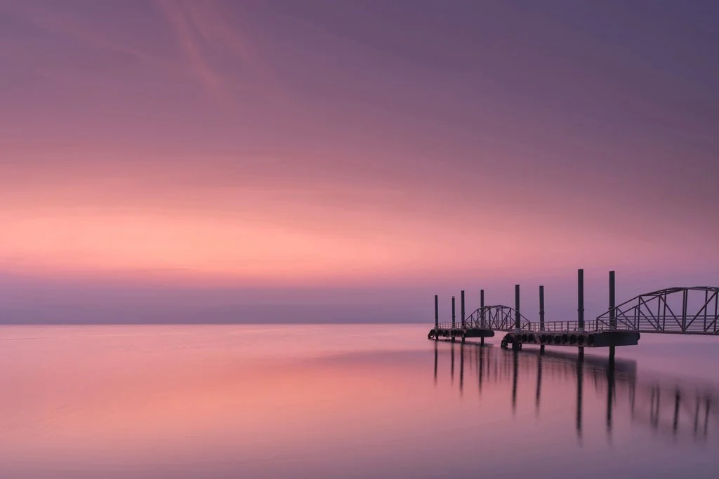 Long-exposure seascape with a pier reflected in still water at sunrise.jpg
