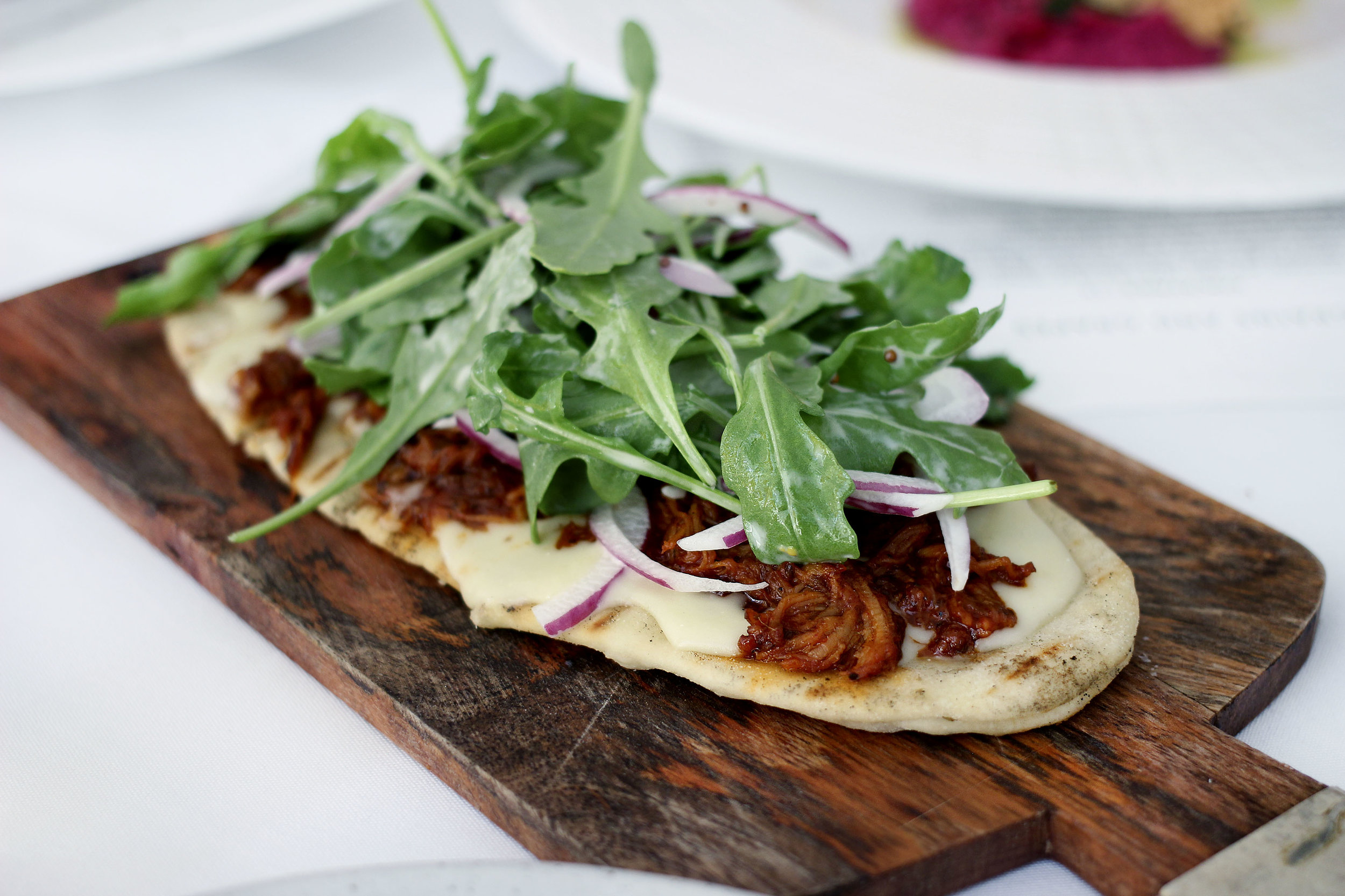 BBQ Flat Bread - Grilled Flatbread, smoky barbeque pulled pork, white cheddar, arugula and red onions.