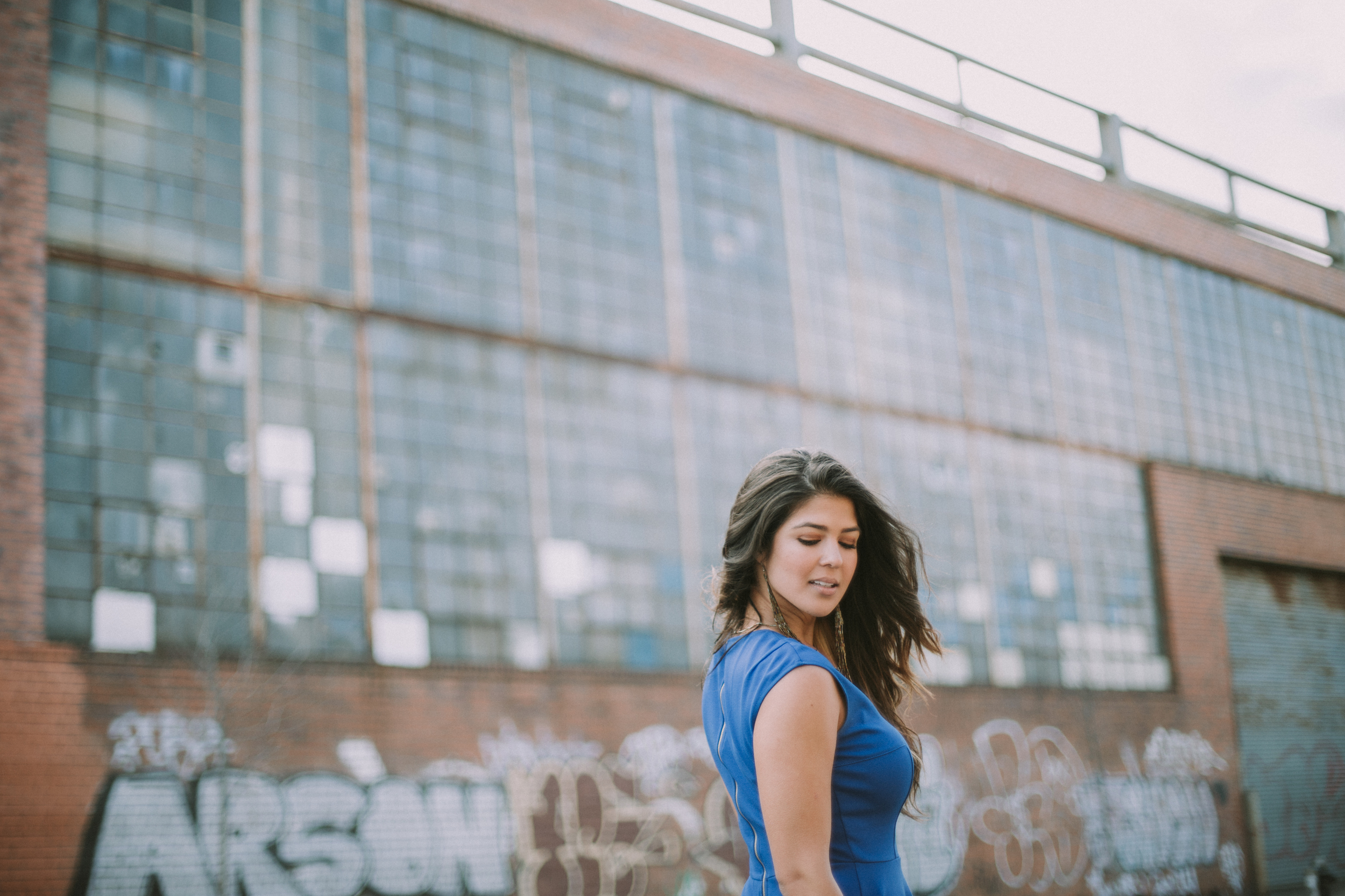 girl in front of industrial graffiti warehouse