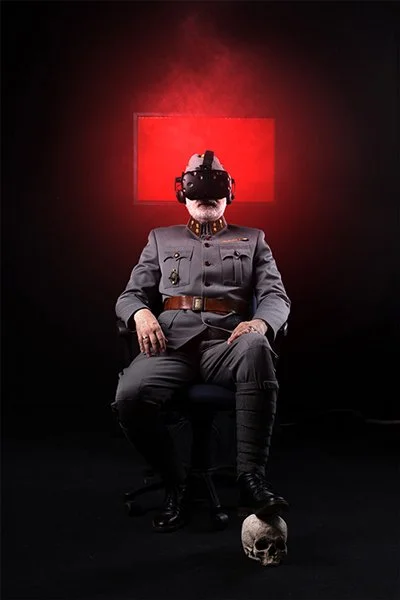 Fotomontage einer Heiligenfigur. Ein älterer Mann in KuK Uniform sitz auf einem Gamingsessel. Er trägt eine VR-Brille und sein linker Stiefel ruht auf einem Totenschädel.