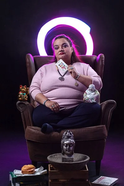 Photomontage einer Heiligenfigur.  Eine füllige Frau sitzt mit gekreuzten Beinen auf einem Ledersessel, umgeben von Statuen und Büchern. Sie hält Tarotkarten in der Hand.