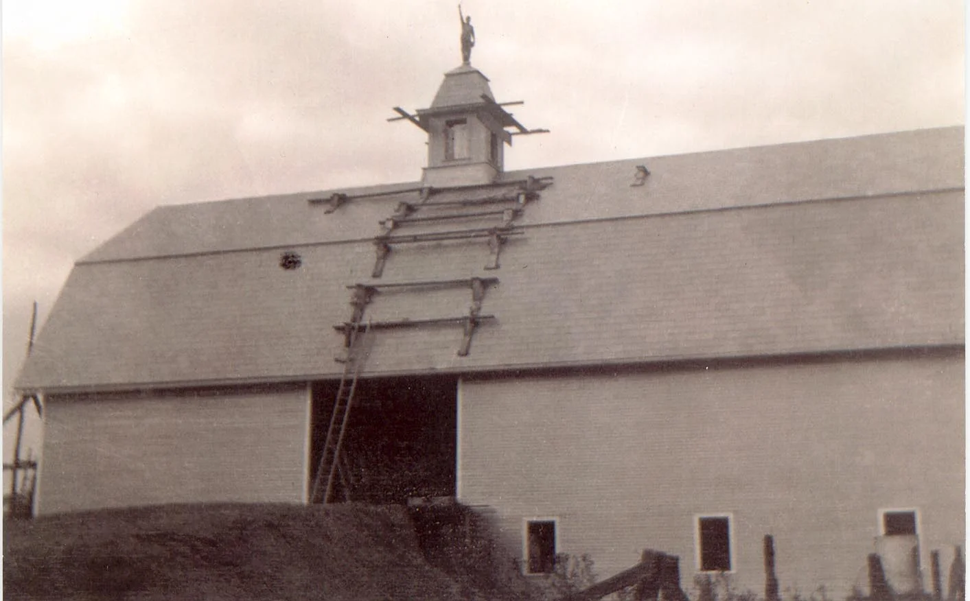 The barn burned to the ground in April, and by August, it was rebuilt. Record time! Here, a worker stands victoriously atop the cupola - brave, but not wise!