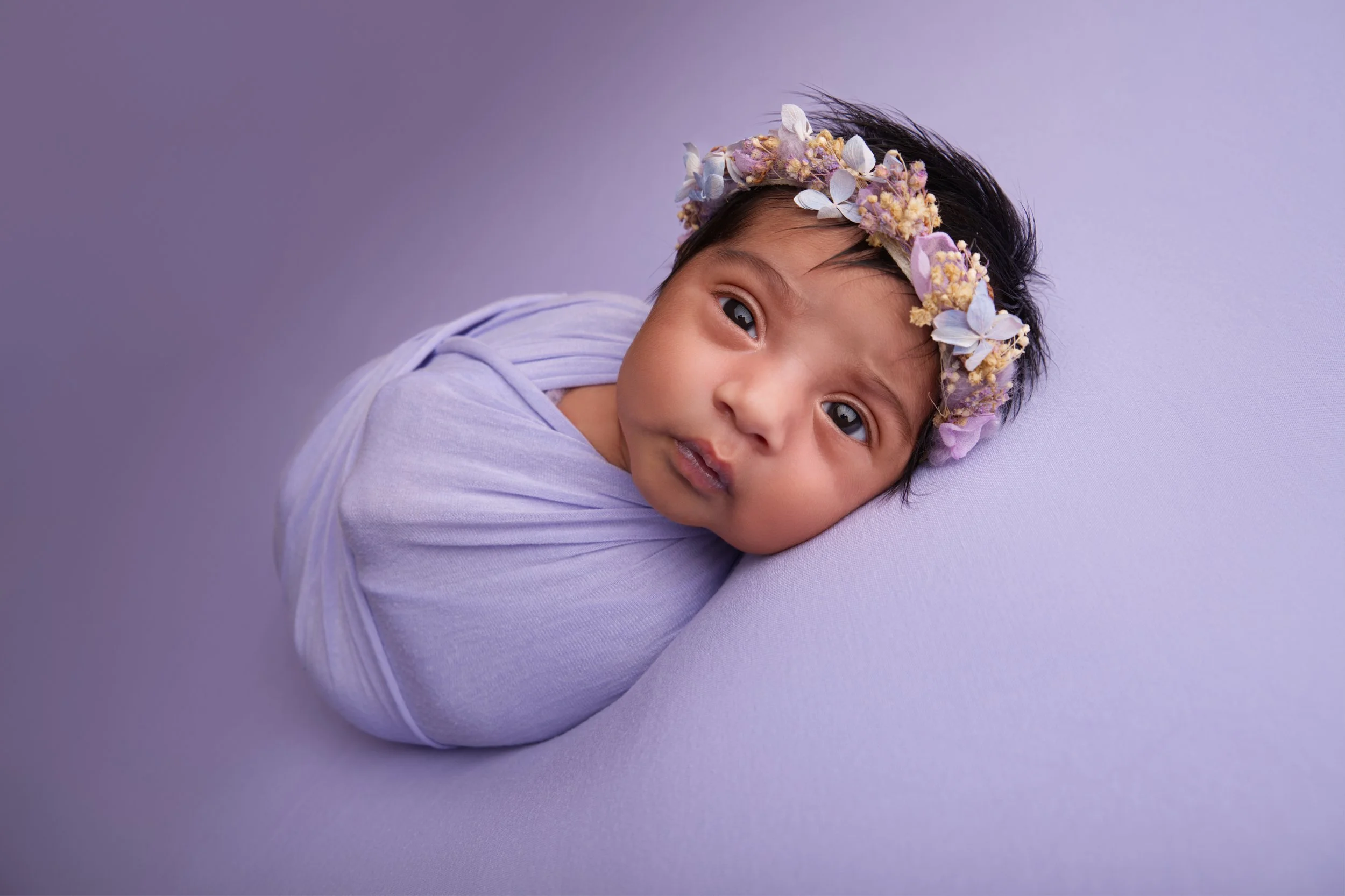 Baby girl on lilac blanket with flower halo