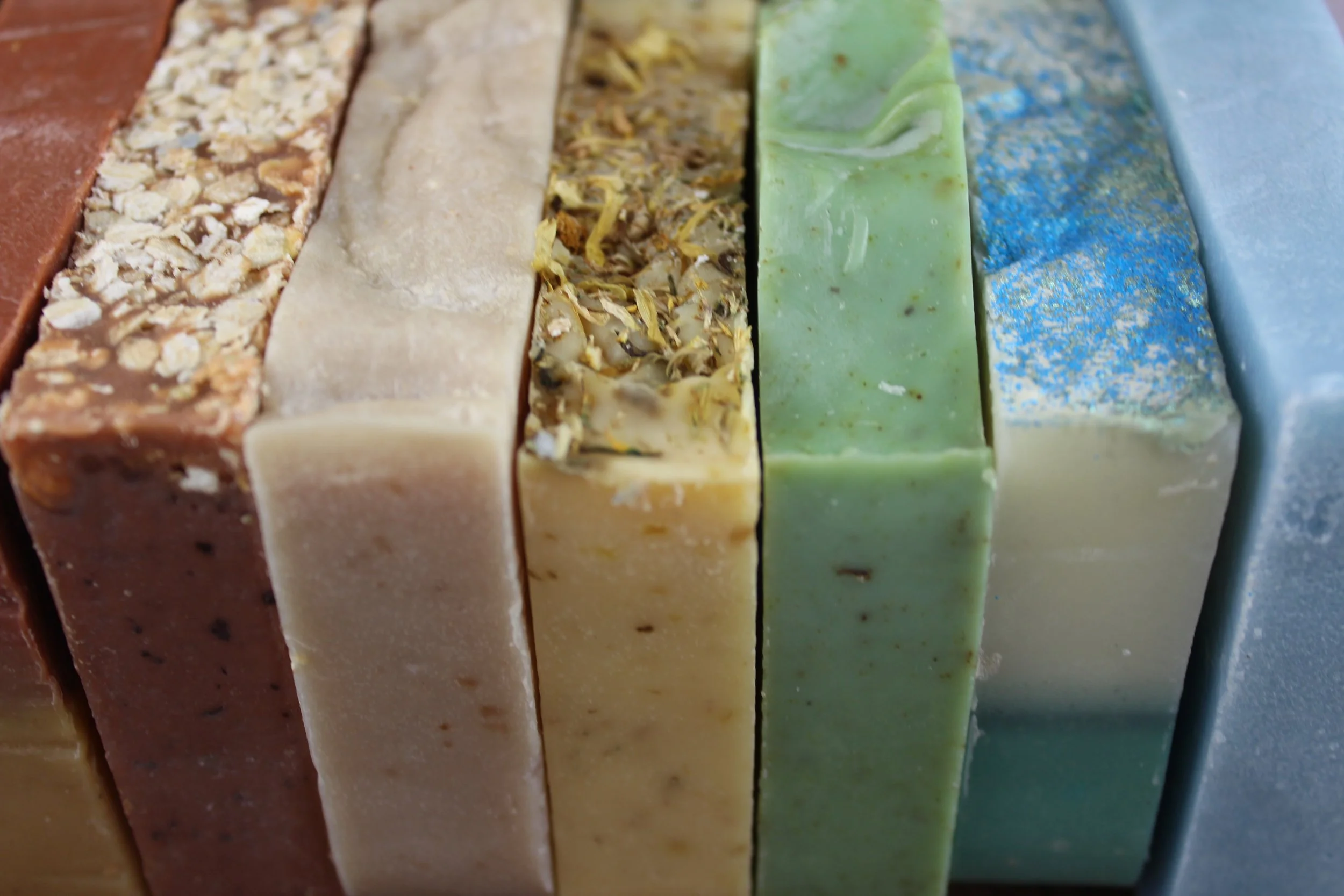 A row of small batch artisan cold process soaps. The soaps have a variety of color and texture.