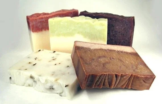 A group of artisan cold process soaps. Five soaps are pictured with various textures and scents including lavender and frankincense and myrrh soap