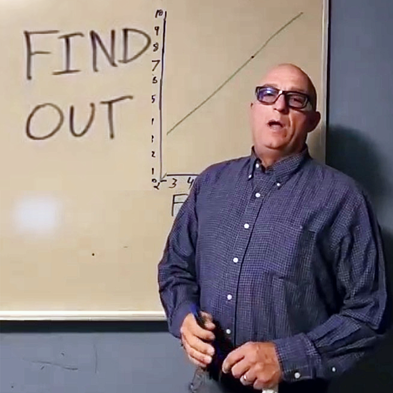 A man wearing glasses and a checkered shirt standing in front of a whiteboard with a graph and the words "FIND OUT" written on it.