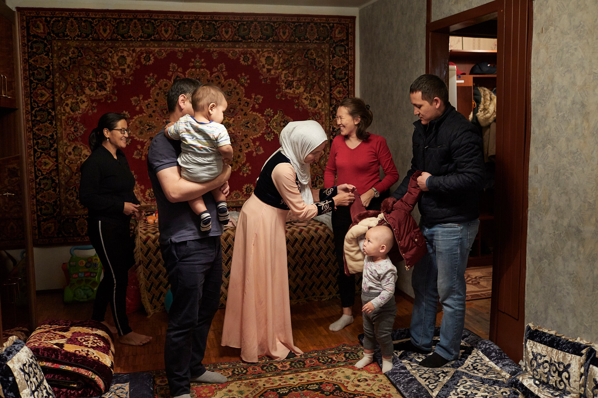 Russia, Moscow, 07/10/2019. Shahrizada Adanova (center, in hijab) welcomes friends at her home in Moscow to celebrate husband Kurmanek Shermatov’s (at left, holding their son Kagan) birthday. Shahrizada first came to Russia from Kyrgyzstan when she