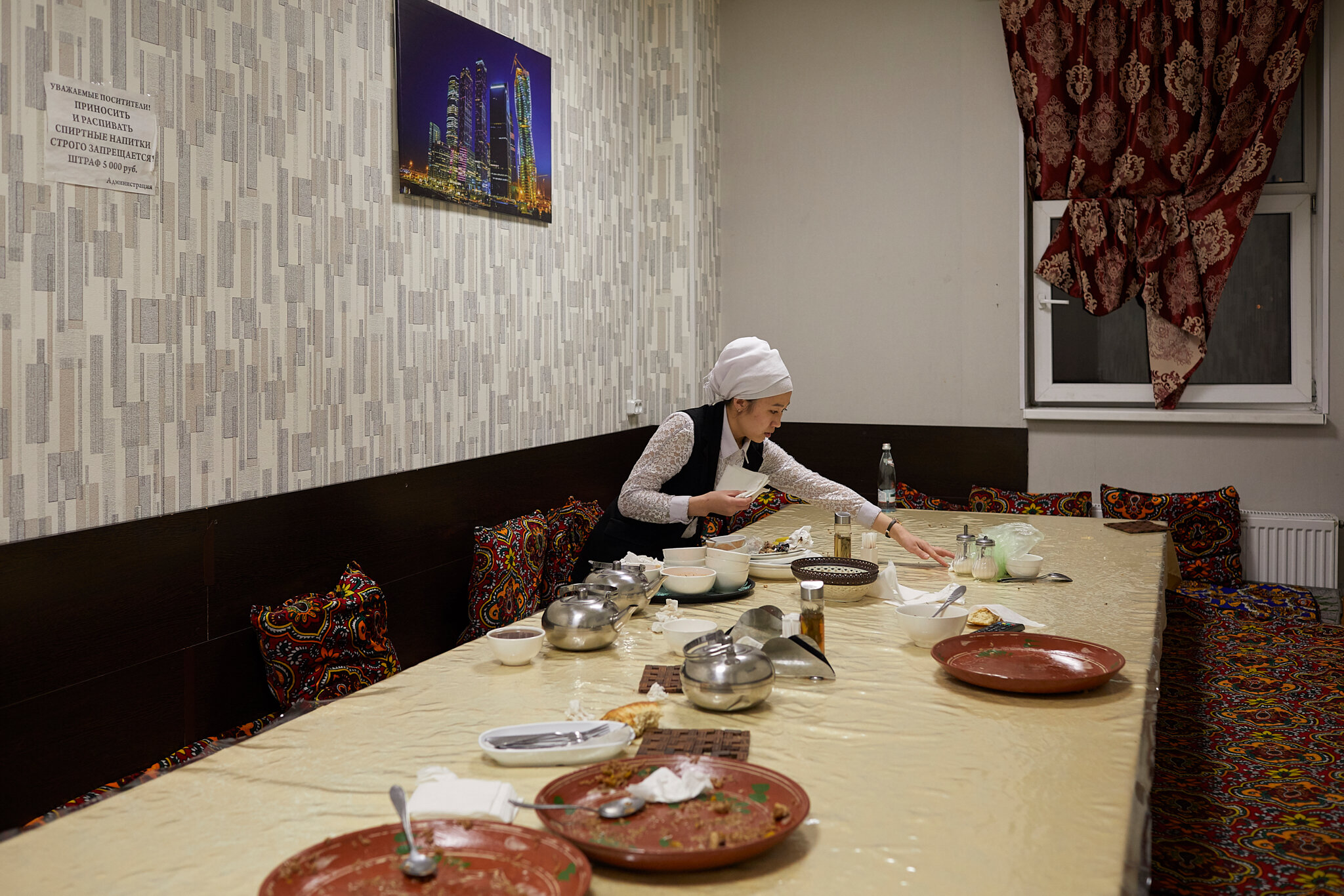  Russia, Moscow, chaikhana “Uzgen”, 04/10/2019. Tahmina K., 25, cleans the room after the guests. The chaikhana “Uzgen” consists of separate rooms. Each room is decorated with traditional carpets “Toshok” and pillows. The chaikhana “Uzgen” is open 24