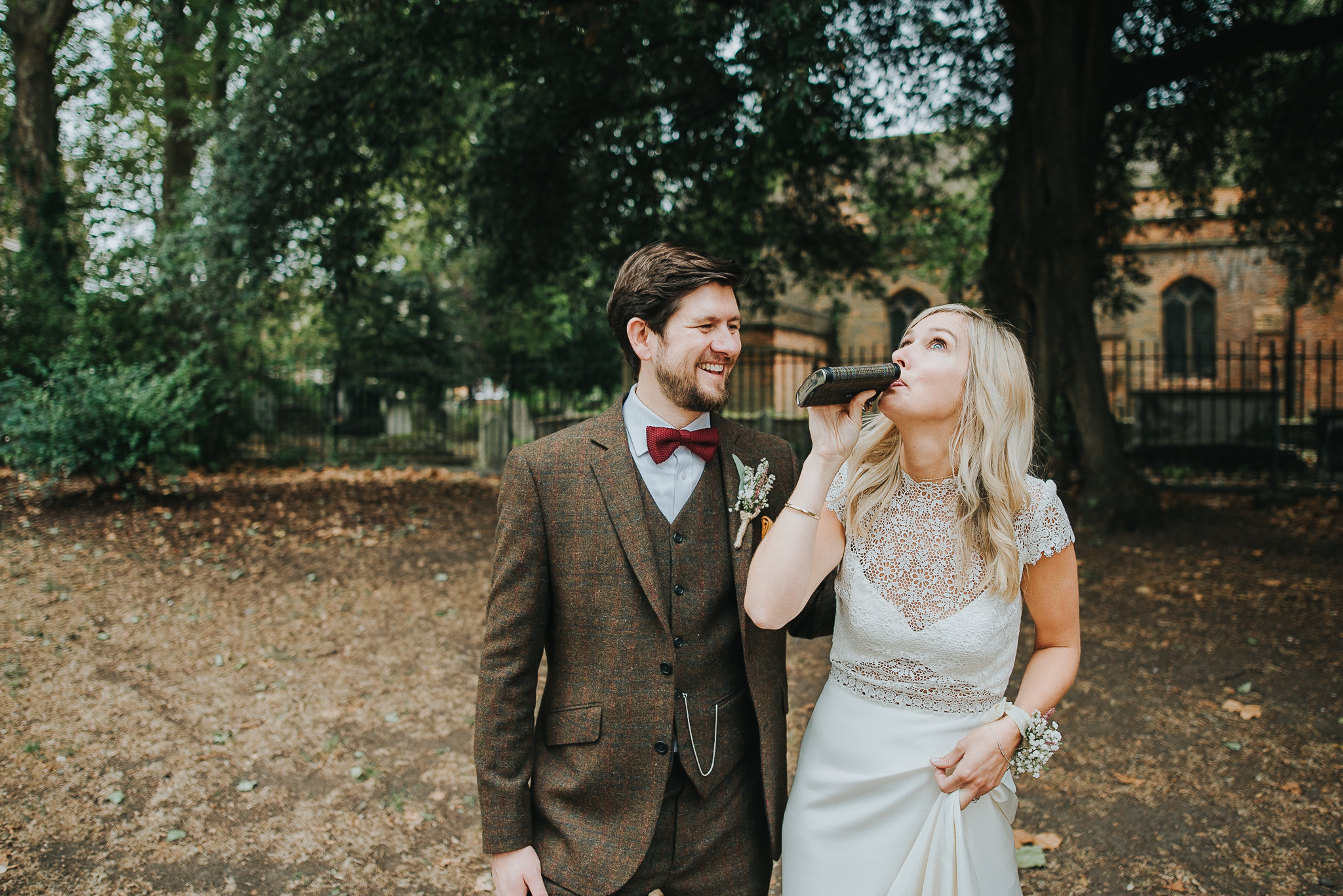 Bride and groom drinking whiskey from hip flask in Clissold Park on their wedding day