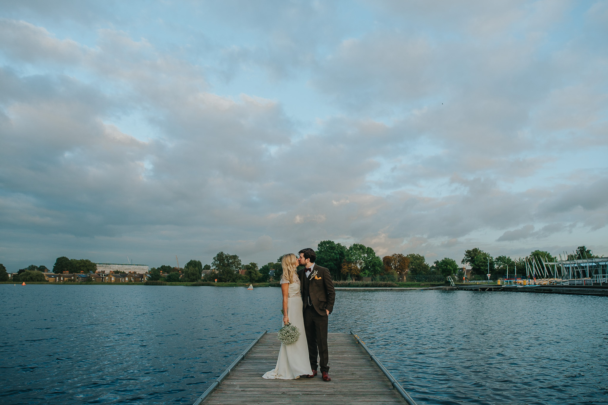 Bride and groom at wedding reception kissing on jetty at Stoke Newington West Reservoir Centre at sunset