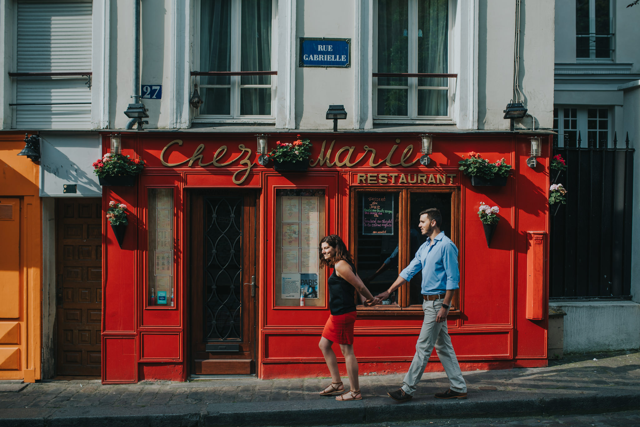 Engagement photoshoot couple in love walking by red Paris cafe on Montmartre street