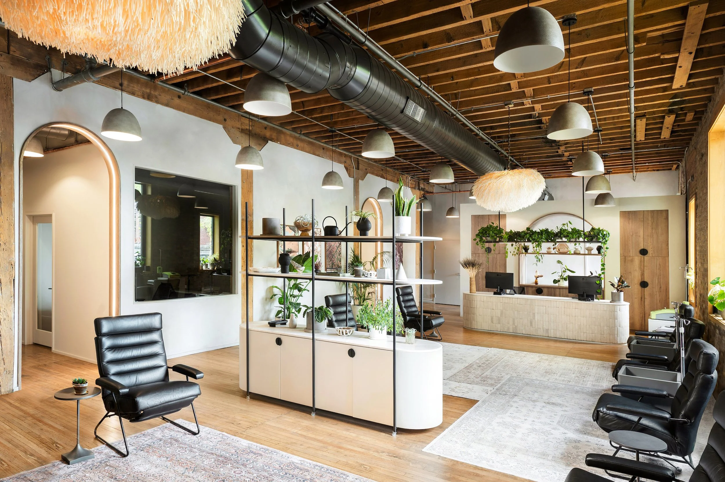 Modern office with wooden accents, black chairs, and lots of greenery and plants, with a reception desk in the background.