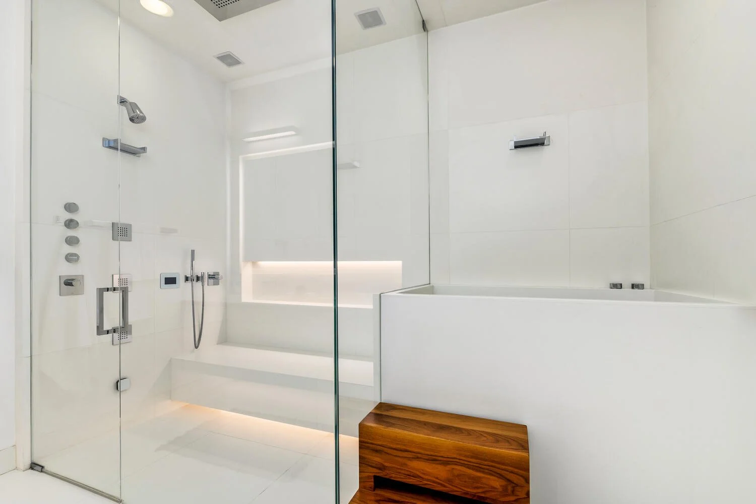Modern bathroom with a glass-enclosed shower area and a white bathtub with wooden steps, minimalistic design, white tiled walls.
