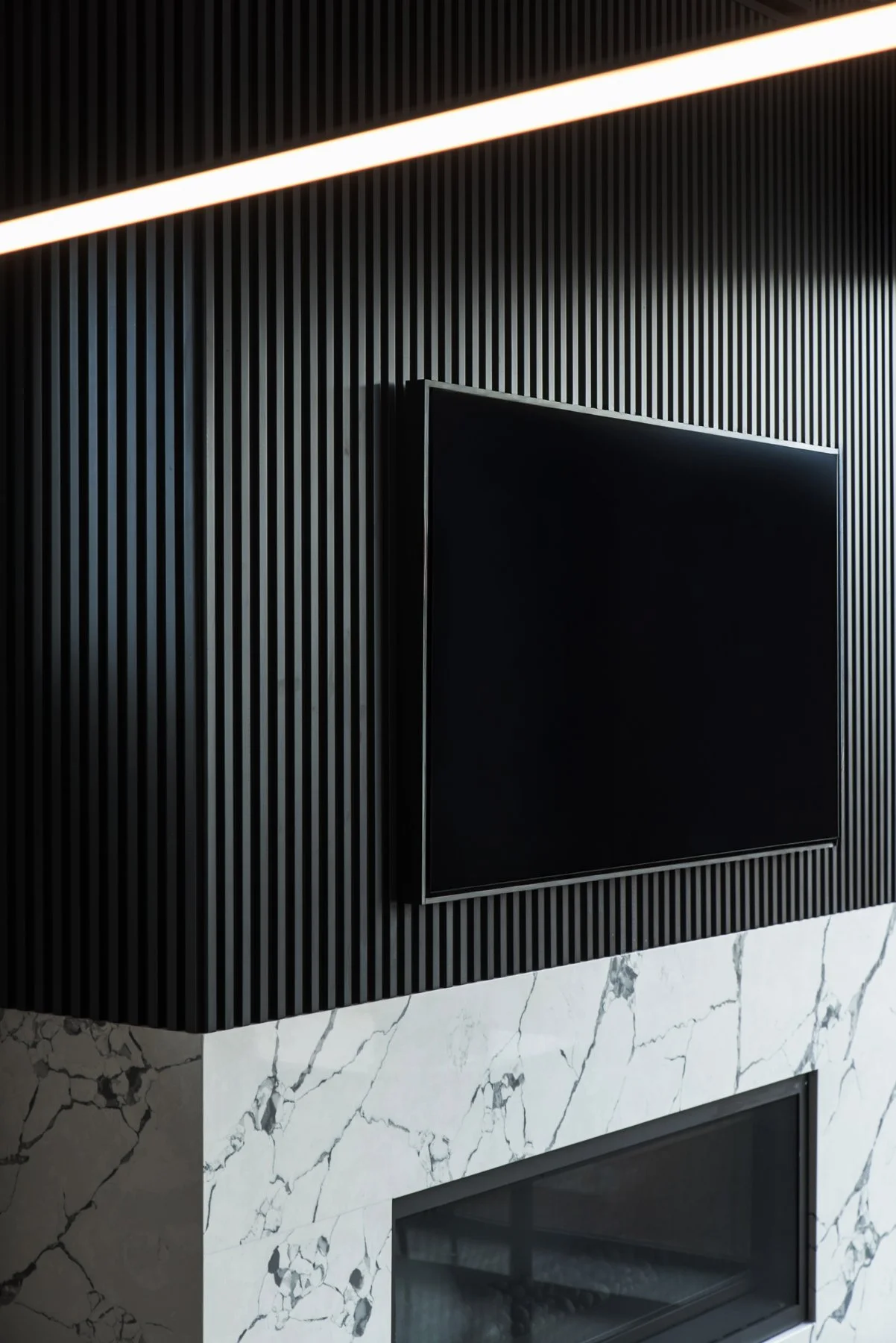 Modern interior with black ribbed fireplace , mounted flat-screen TV, and a superwhite stone fireplace beneath.