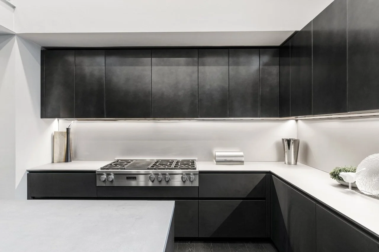 Modern Boffi kitchen with black metal cabinets, stainless steel gas stove, white countertops, and decorative vases and dishes.