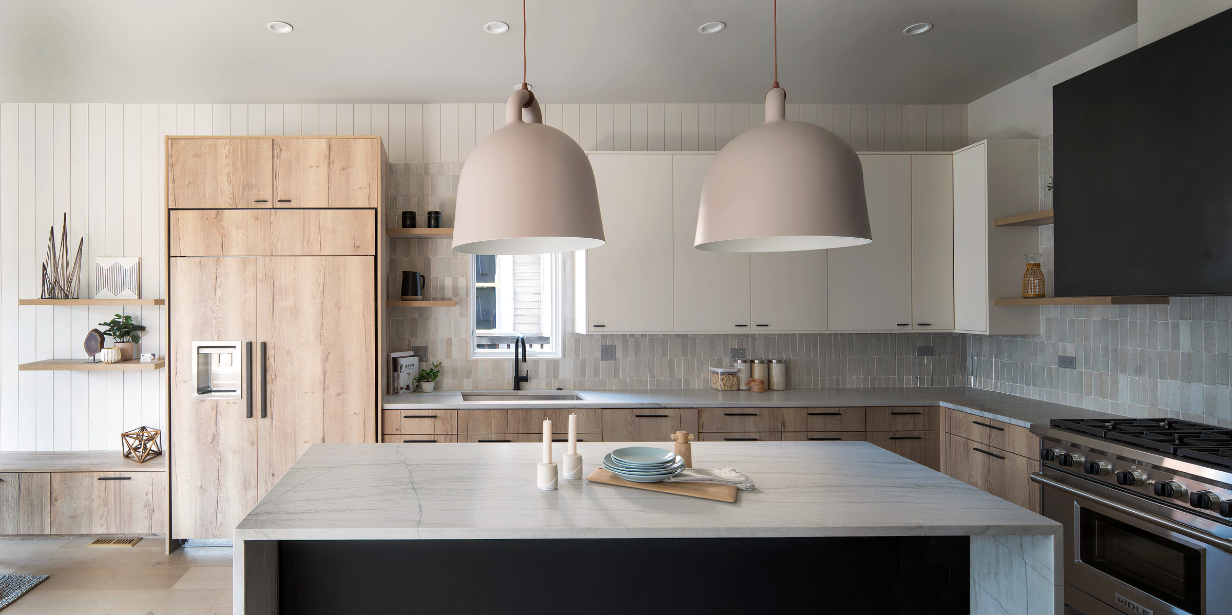 Modern kitchen with white and wood cabinetry, a marble island, large pendant lights, and stainless steel appliances
