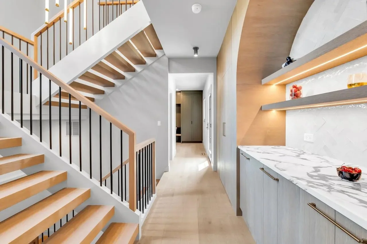 Modern interior hallway with wooden stairs, white walls, and a marble countertop with open shelves holding decorative items.