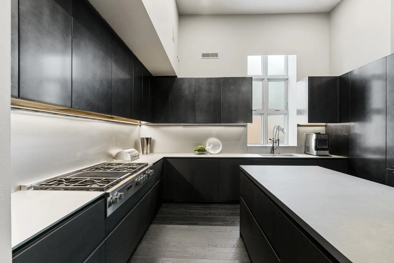 Modern Boffi kitchen with black cabinets, white countertops, a stove, a sink under a window, and a coffee machine.
