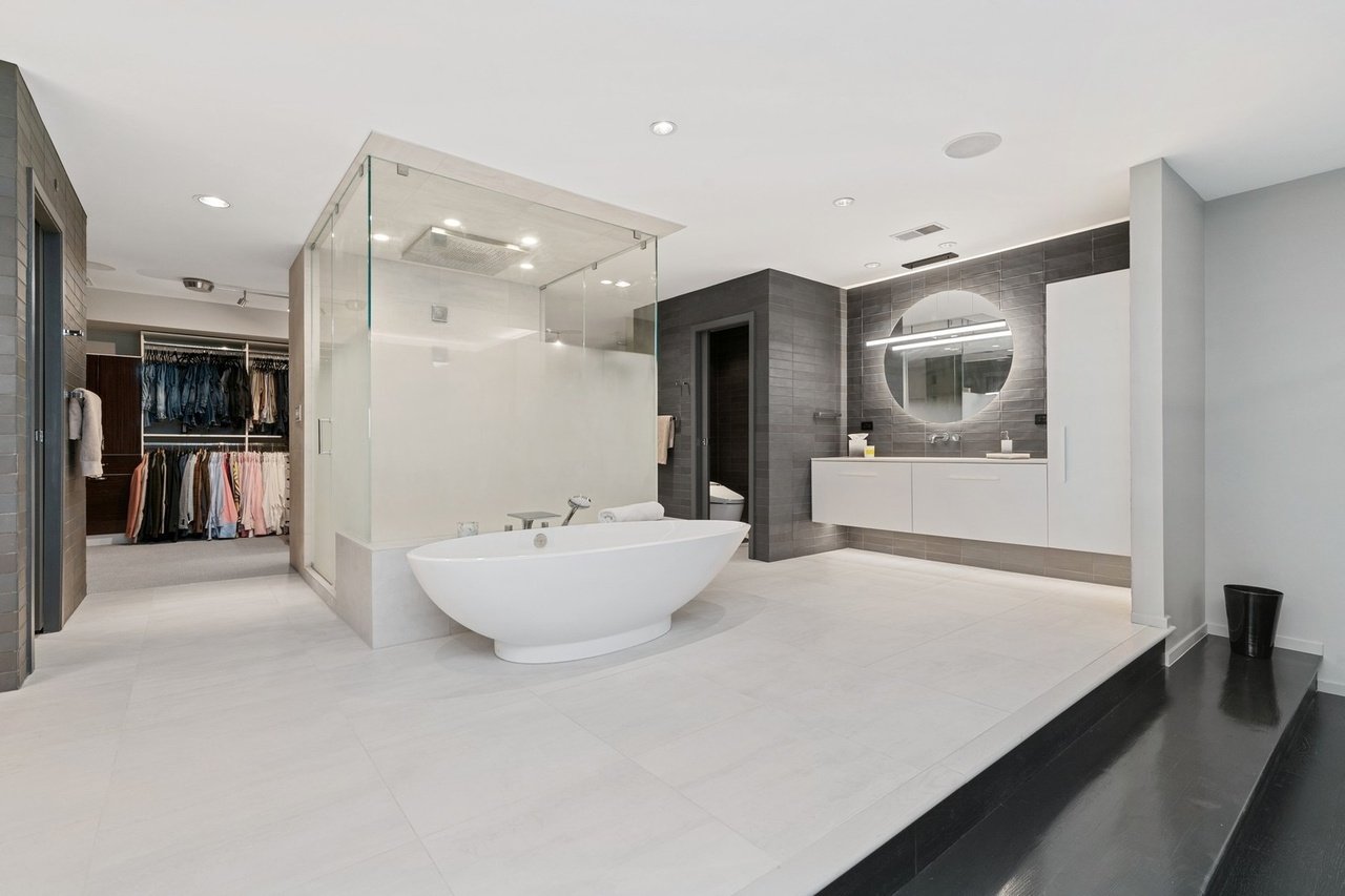 Modern bathroom with a free-standing bathtub, glass shower enclosure, and a vanity with a round mirror.