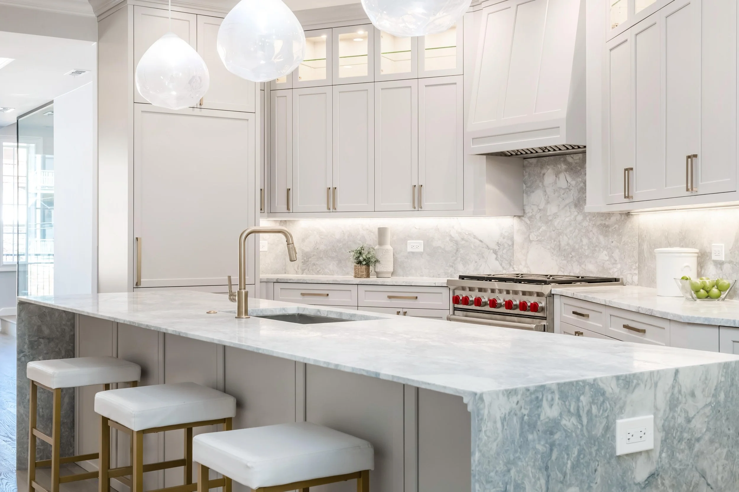 Modern kitchen with white cabinetry, marble countertops, pendant lights, a stove with red knobs, and a kitchen island with seating.