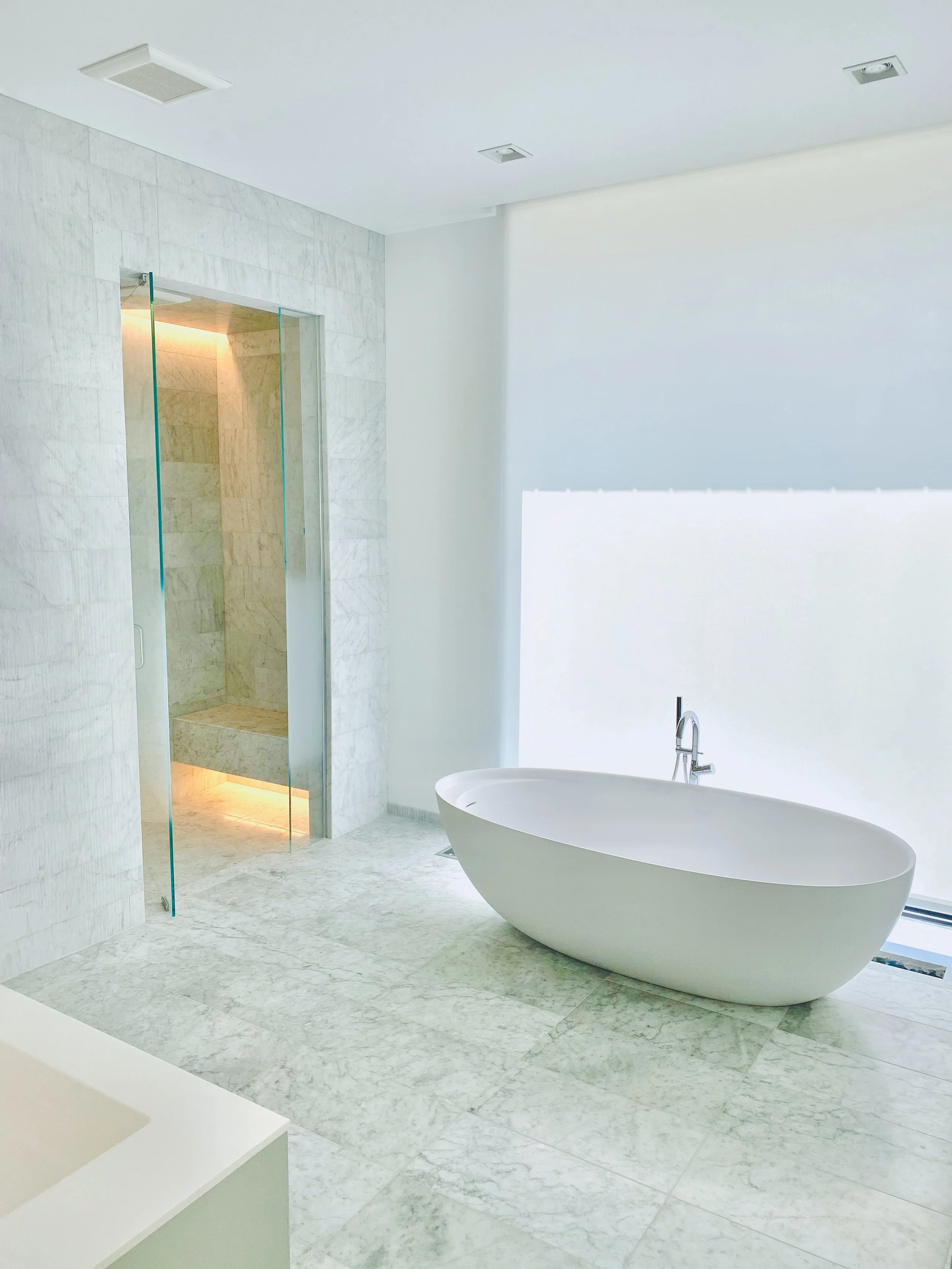 Modern bathroom with a standalone bathtub near a window, a shower with glass doors, and marble tile flooring and walls.