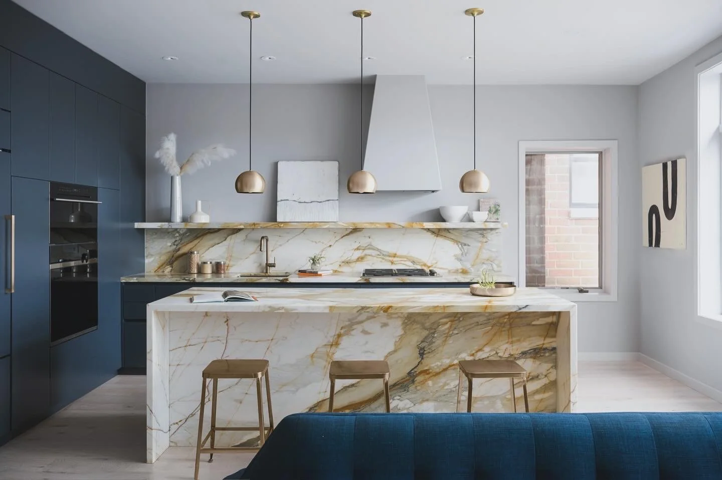 Modern kitchen with a mecchia vecchia marble island and backsplash, dark blue cabinets, and gold pendant lights.