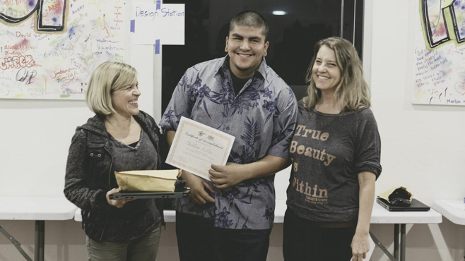 Kathyrn Stellmacher and Lauren Segal present a Certificate of Completion to Project Kinship member Christian Padilla.