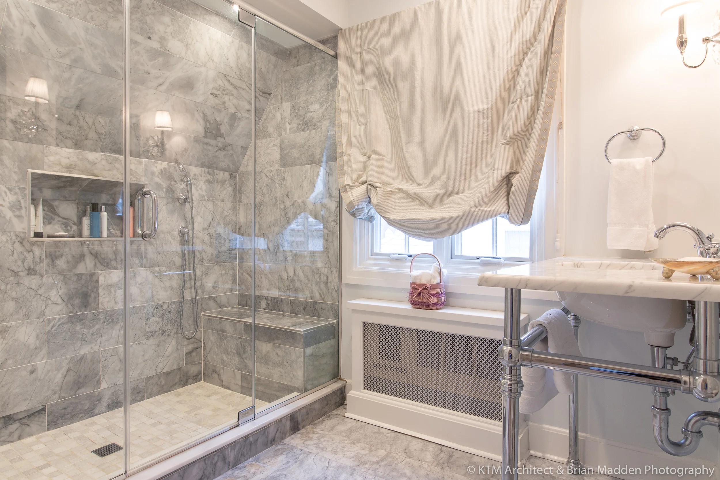 The master bath features a spacious marble shower with seating, a marble-topped console vanity that helps the bathroom retain an open feel, and a toilet area with built-in storage shelving.