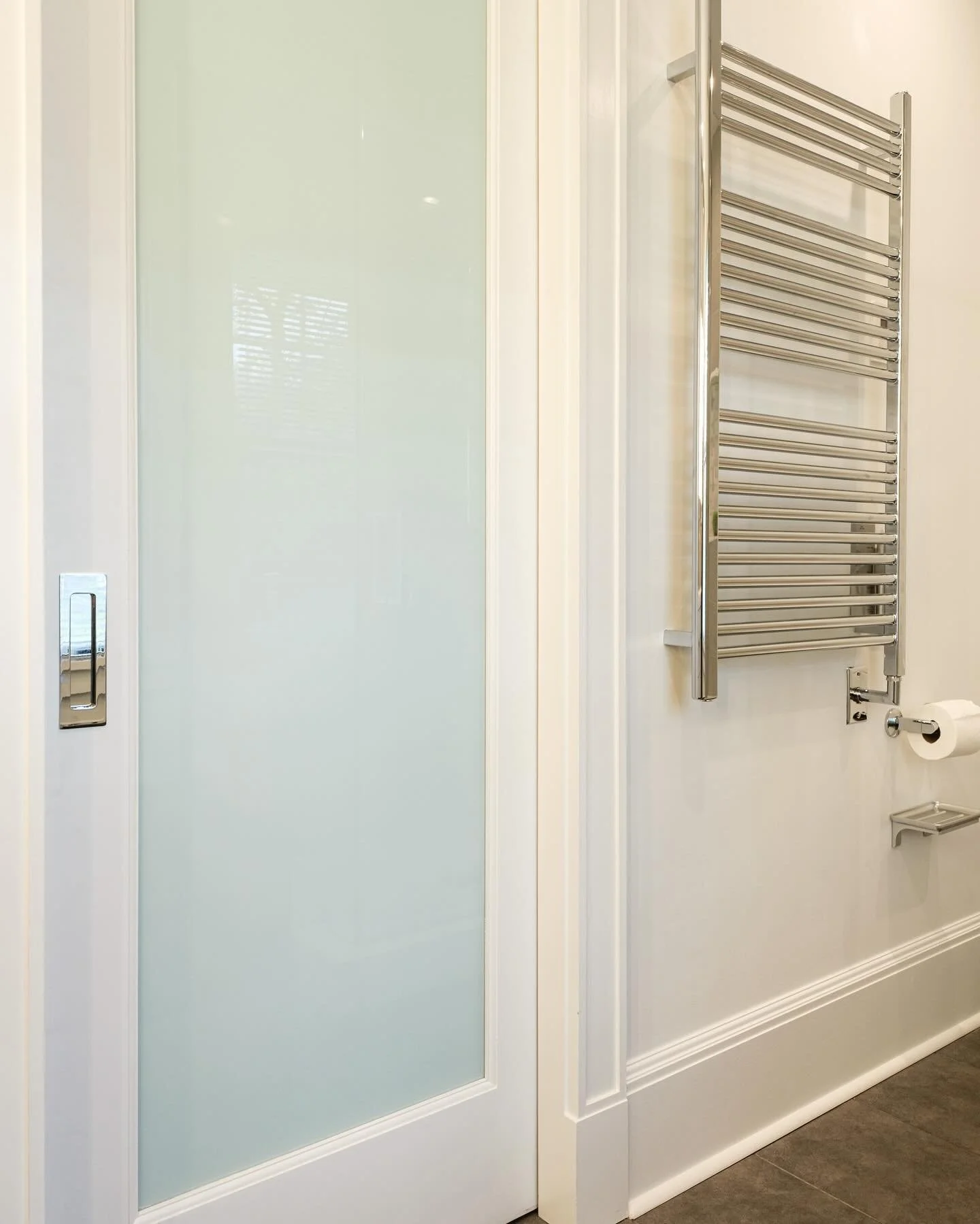 A modern primary bath renovation with pocket doors, towel warmer and soft gray colors contrasted with crisp whites. #bathroomdesign #modern #smallbutmighty #smallspacedesign #renovation #larchmontny @ktmarchitect photos by @maddenstudio