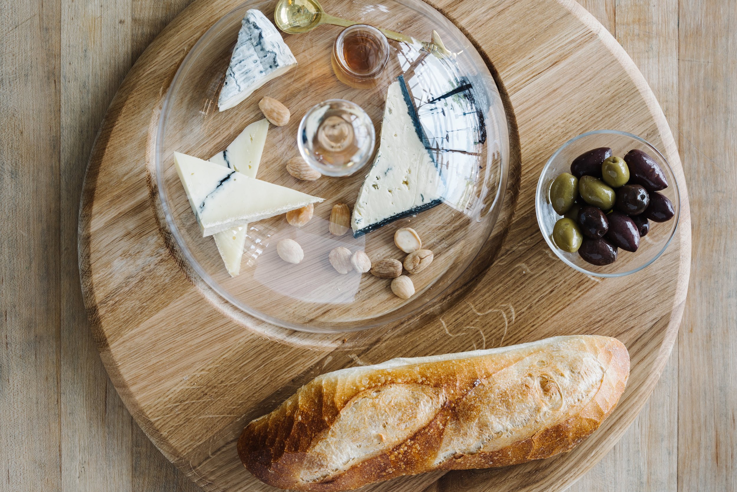 Cheese, olives, and baguette on round wood board