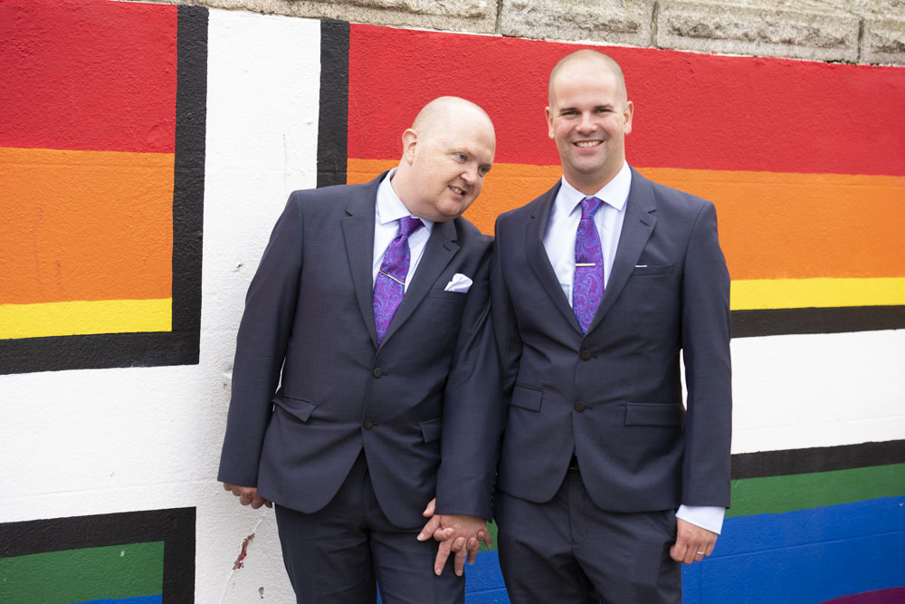 Grooms in front of pride wall