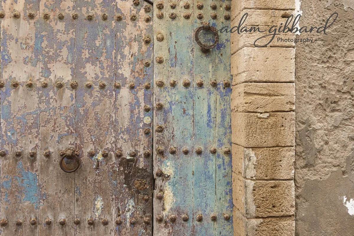 Old, rusty metal door with blue and brown paint, surrounded by a brick and stone wall.