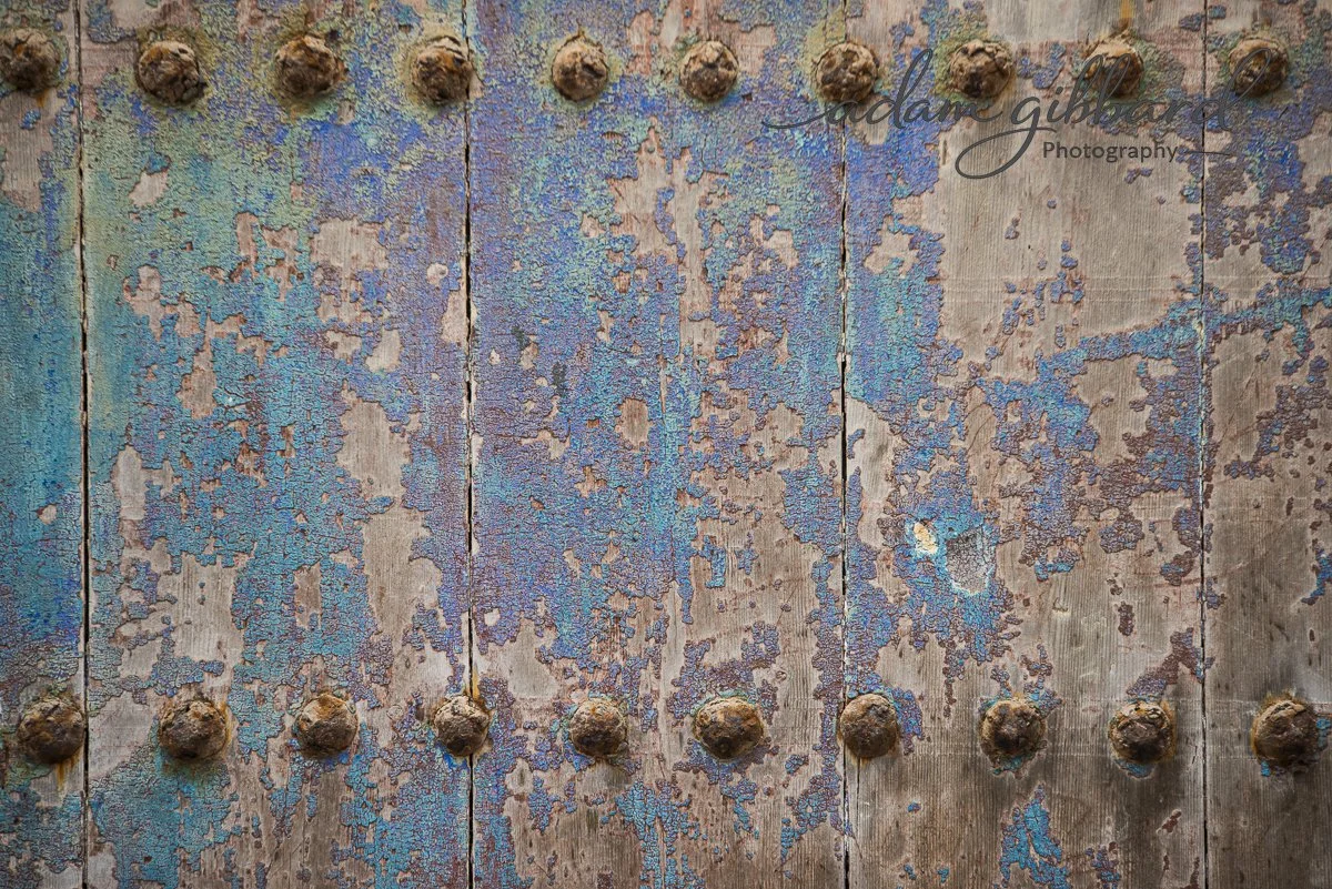 Close-up of a weathered wooden surface with peeling blue paint and rusted metal bolts.