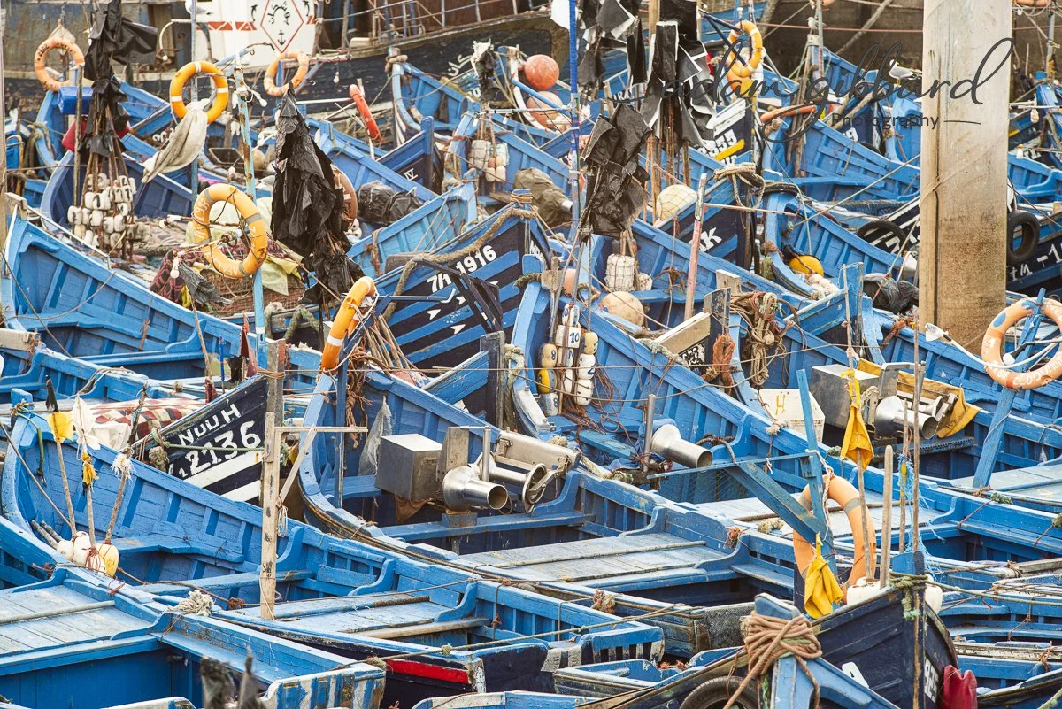 A cluttered scene of numerous small blue boats stacked and tied together, with life preservers, ropes, buoys, and other boating equipment attached.